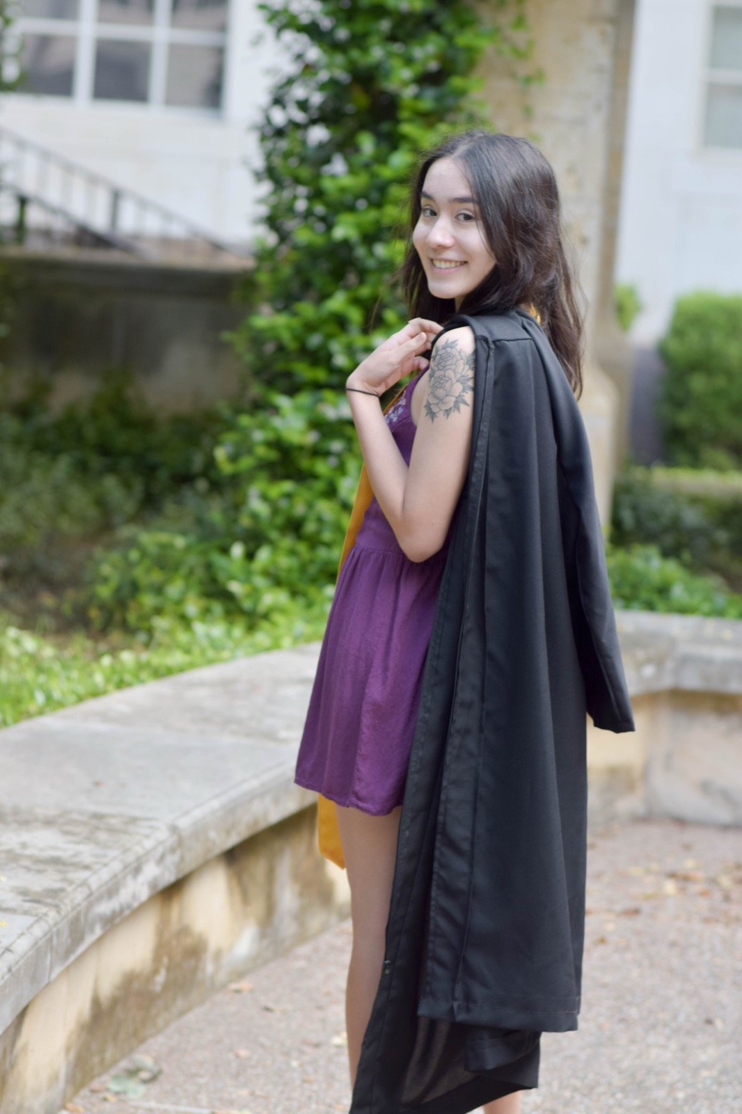 A woman glances back over her shoulder, laughing, with a black graduation gown draped over one arm.
